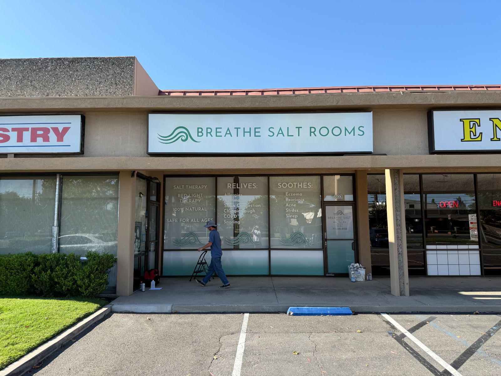 Breathe Salt Rooms storefront: a white fascia sign with a green wave logo above windows filled with cut and printed vinyl listing services and benefits, plus a wave motif along the glass, installed by Hi Sign, Brea, CA