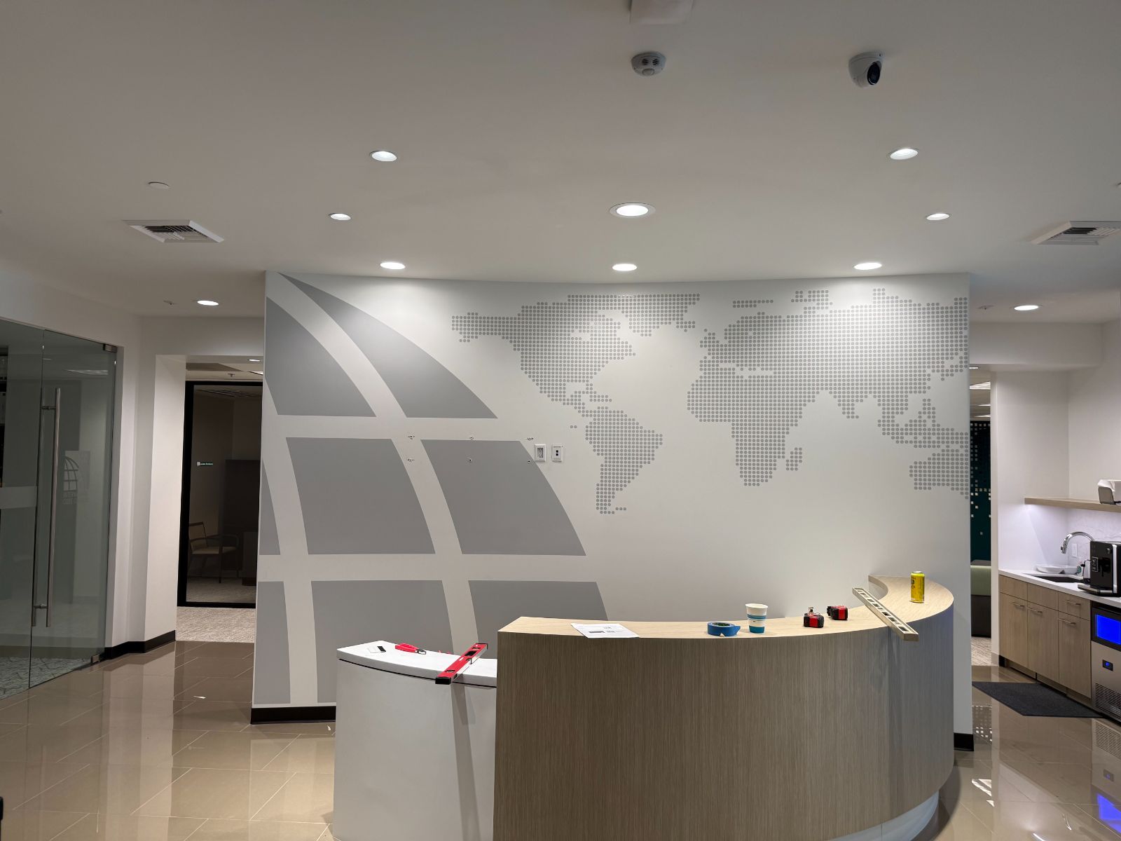 Curved reception wall behind a front desk with a large gray graphic: a dotted world map and sweeping globe grid lines applied in printed and cut vinyl to the interior wall, installed by Hi Sign, Brea, CA