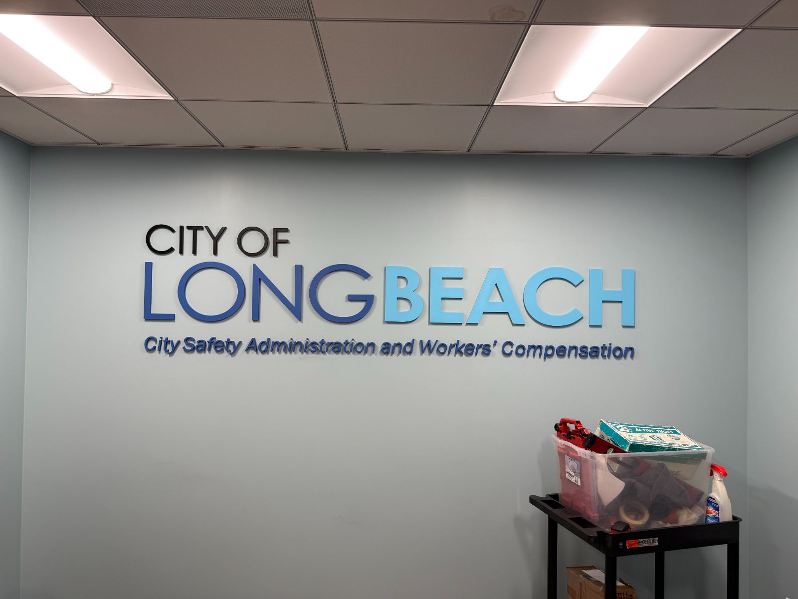 Interior wall with 'City of Long Beach' in dimensional letters: black, blue and light-blue faces above a line reading 'City Safety Administration and Workers' Compensation,' flush-mounted on a pale wall, installed by Hi Sign, Brea, CA