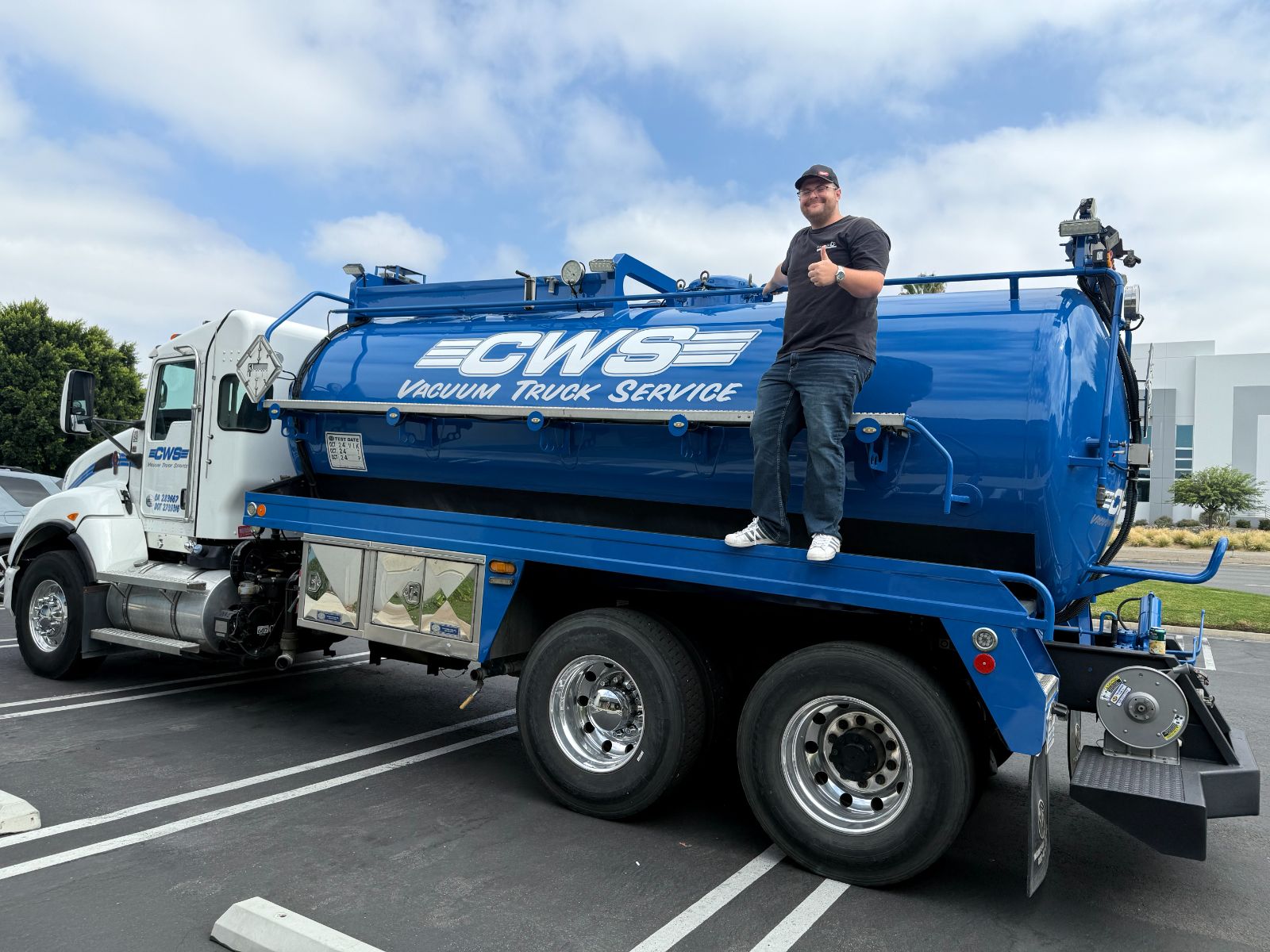 Blue CWS vacuum tanker truck in a parking lot with a man standing on the deck giving a thumbs up: large white 'CWS Vacuum Truck Service' vinyl graphics along the tank, installed by Hi Sign, Brea, CA