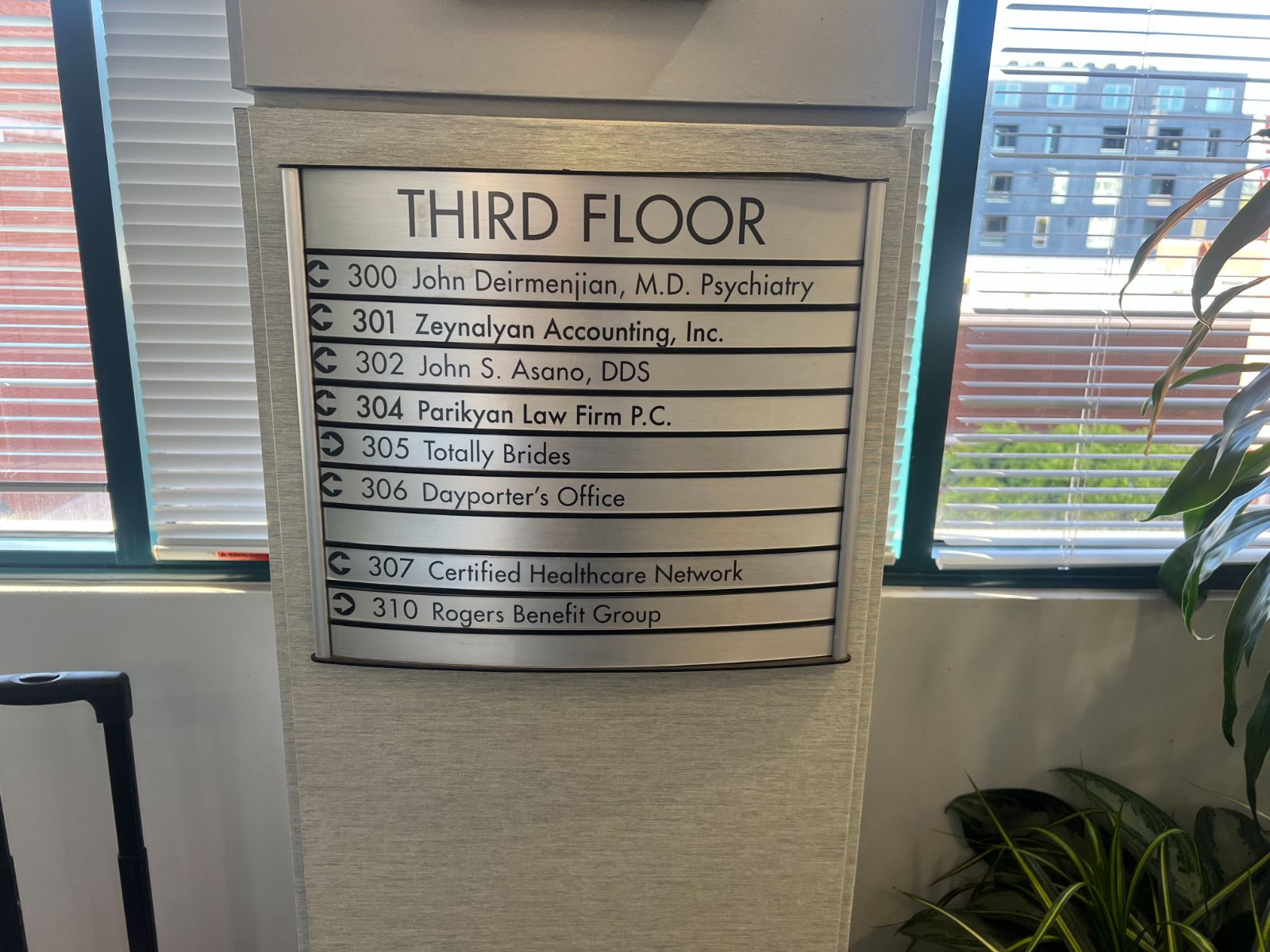 Brushed-aluminum tenant directory headed 'Third Floor,' listing suite numbers and business names on updatable insert strips with directional arrows, mounted by a window, installed by Hi Sign, Brea, CA