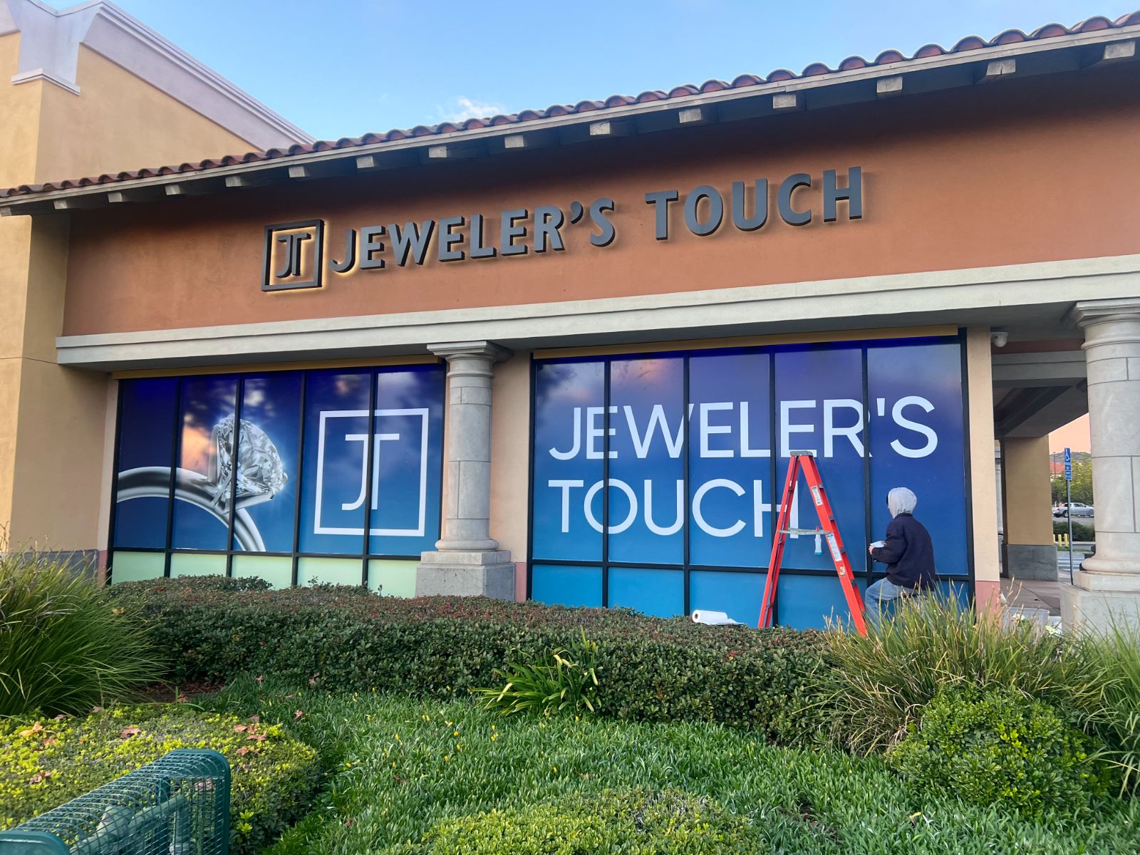 Jeweler's Touch storefront: dark dimensional letters and logo on the stucco fascia above windows fully covered in blue printed vinyl graphics showing a diamond ring and the store name, installed by Hi Sign, Brea, CA