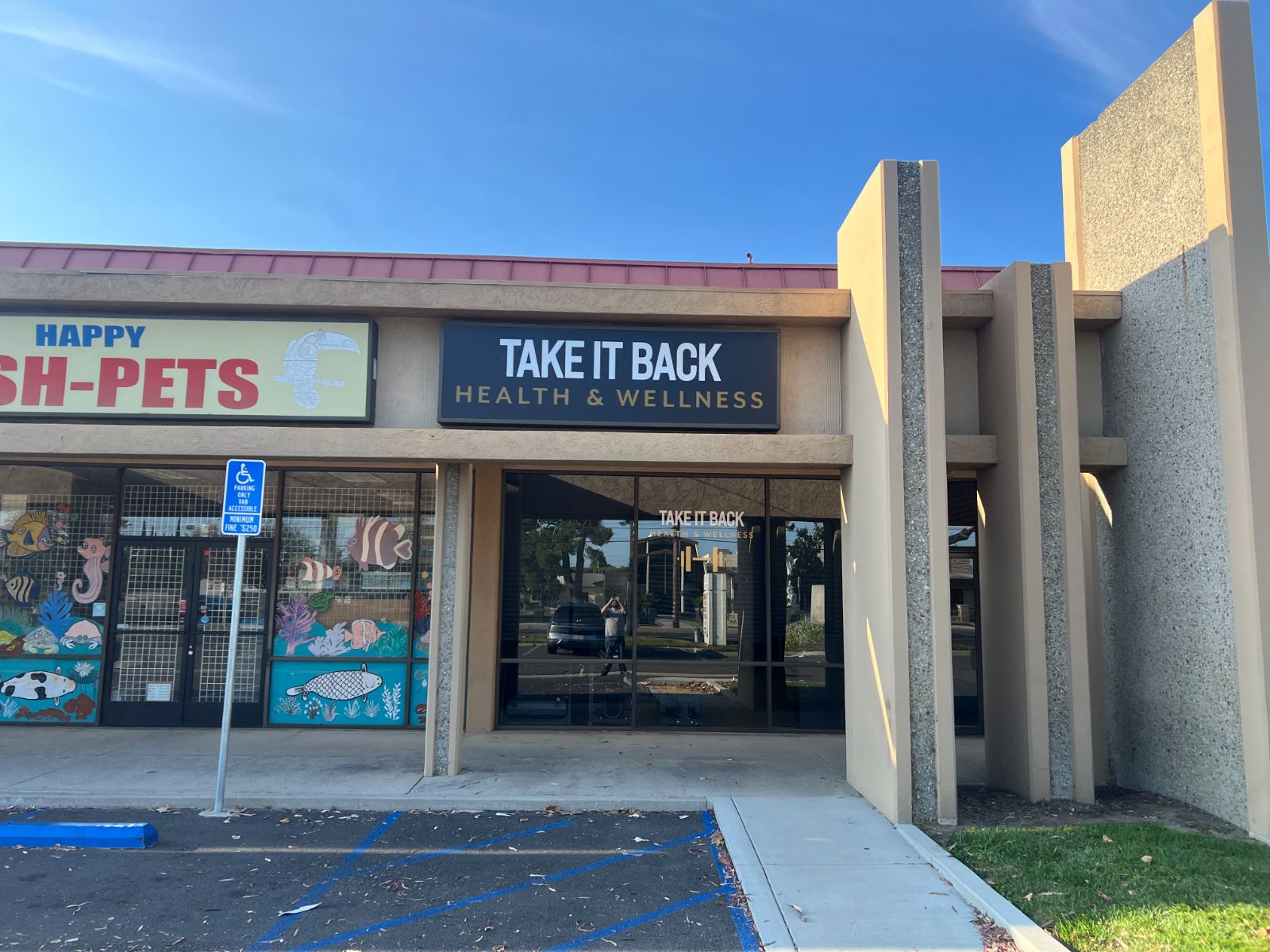 Storefront fascia sign cabinet reading 'Take It Back: Health & Wellness' in white and gold on a black face, mounted above the entrance of a strip-mall unit next to a pet store, installed by Hi Sign, Brea, CA