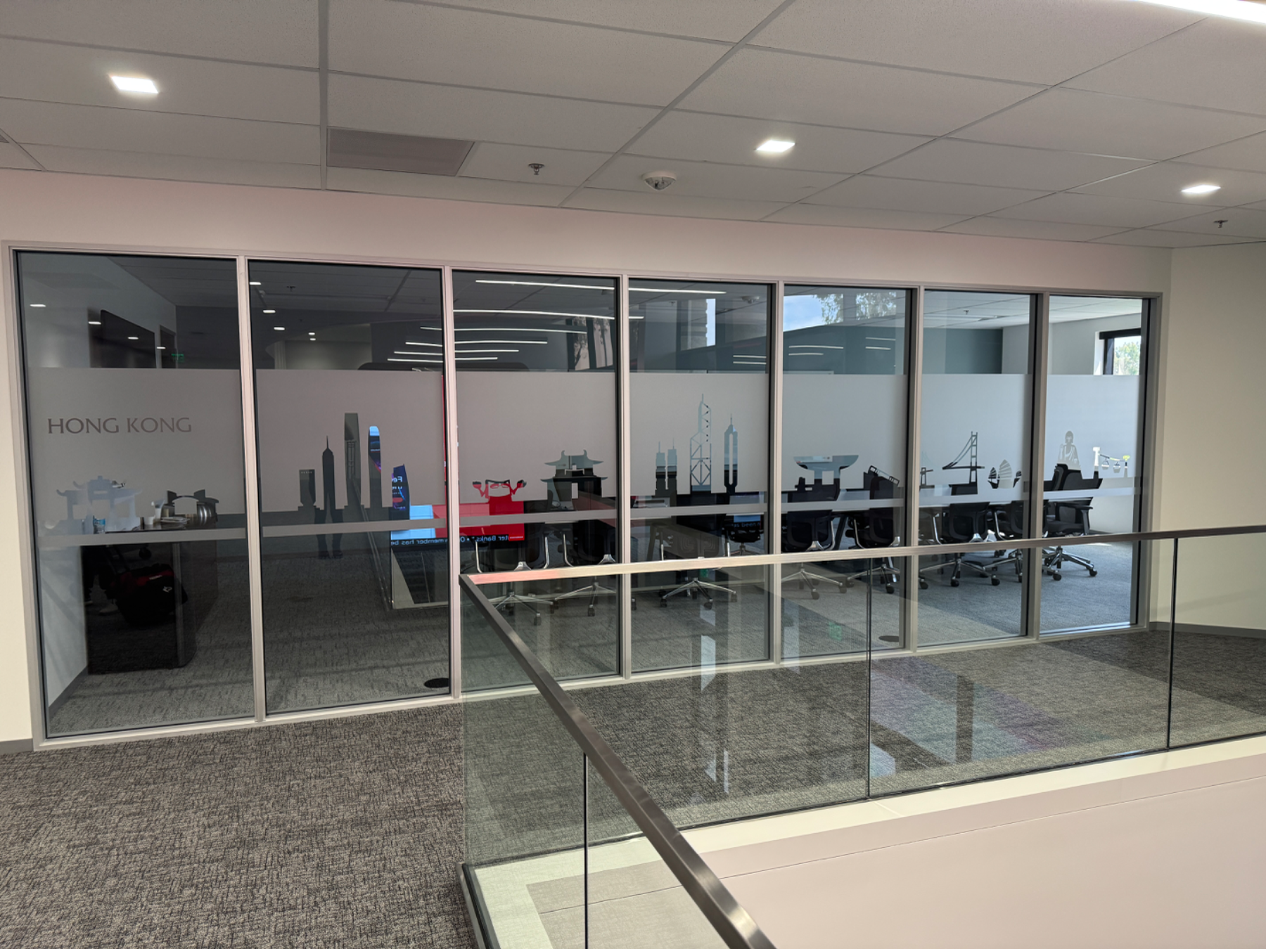 Glass-walled meeting room on an office mezzanine with a frosted privacy band carrying a cut-vinyl Hong Kong skyline and the room name HONG KONG, installed by Hi Sign, Brea, CA