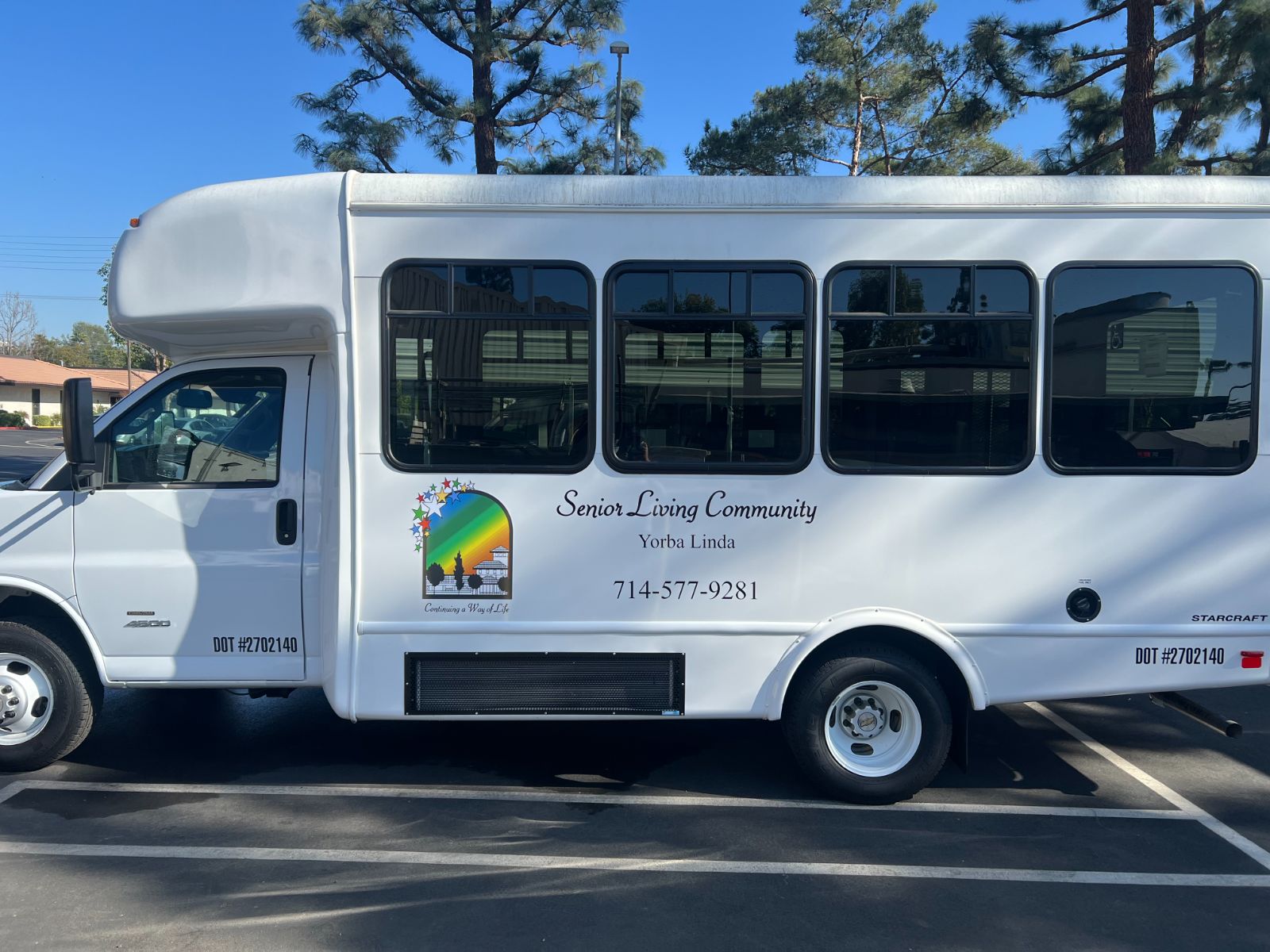 Driver-side vehicle graphics on a white Starcraft shuttle bus for Senior Living Community Yorba Linda: printed vinyl logo and die-cut lettering with business name, city, and phone number on the exterior body panel, installed by Hi Sign, Brea, CA