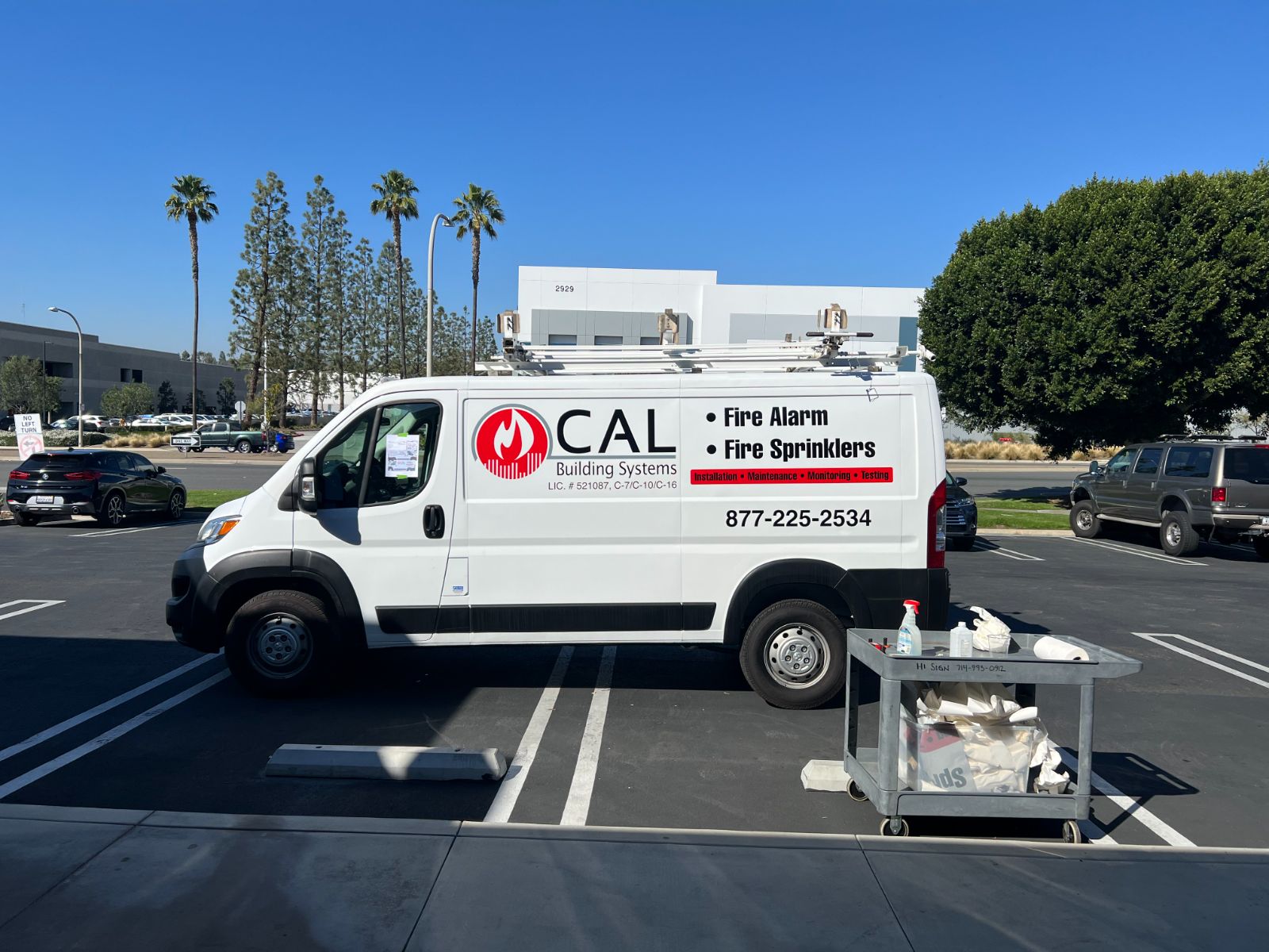 Passenger side of the same white CAL Building Systems van in a parking lot: vinyl logo, 'Fire Alarm / Fire Sprinklers' lettering and phone number on the body panel, installed by Hi Sign, Brea, CA