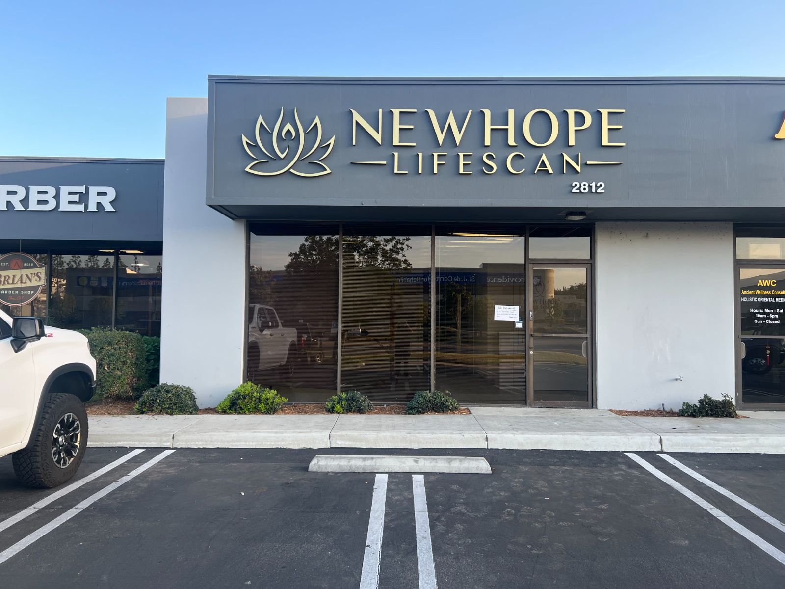 Exterior storefront fascia for NewHope Lifescan: gold-faced dimensional letters spelling the business name beside a gold lotus logo, mounted on a dark gray building band, installed by Hi Sign, Brea, CA