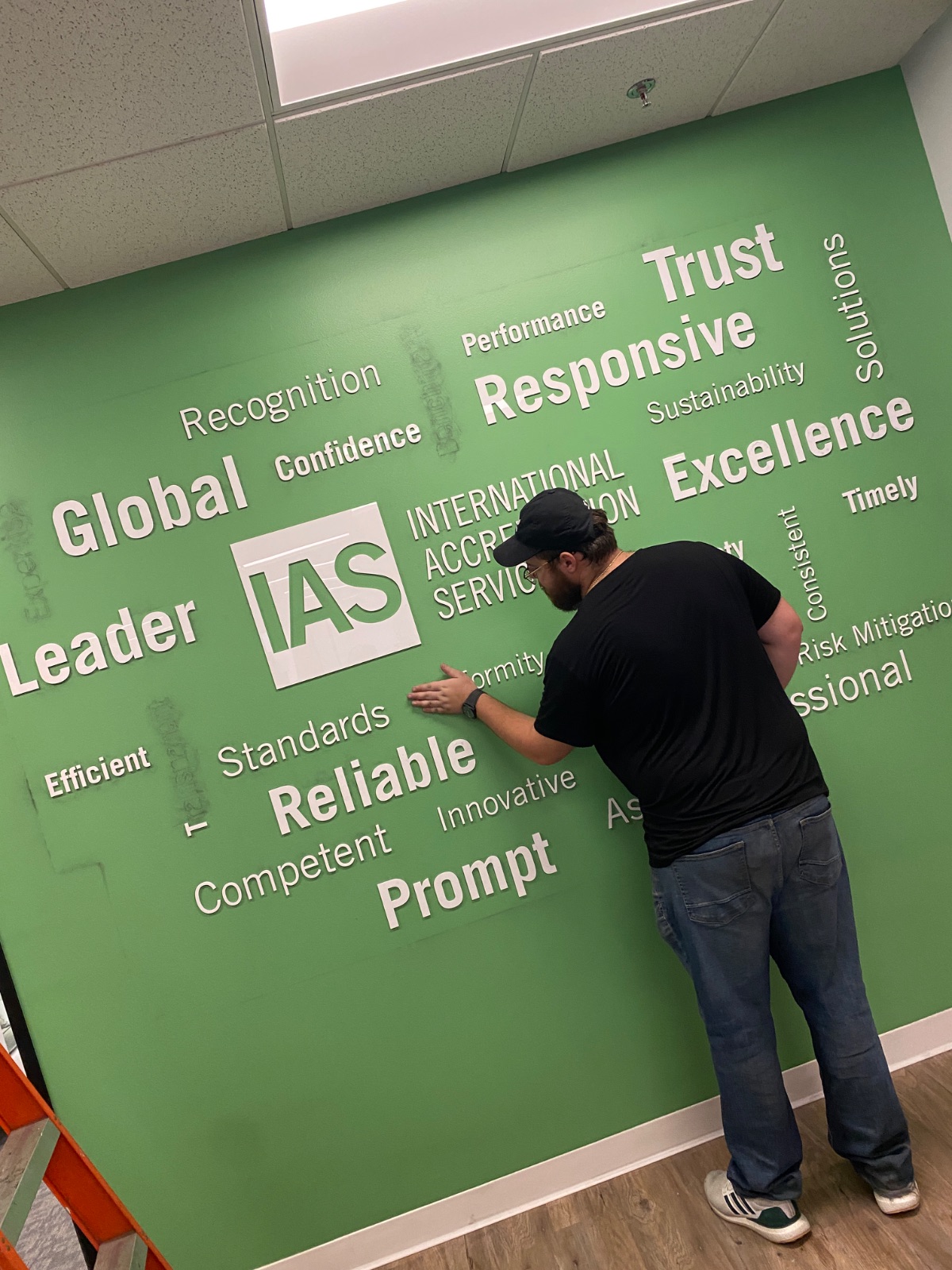 Installer squeegeeing a cut-vinyl word panel onto the green wall during application, installed by Hi Sign, Brea, CA