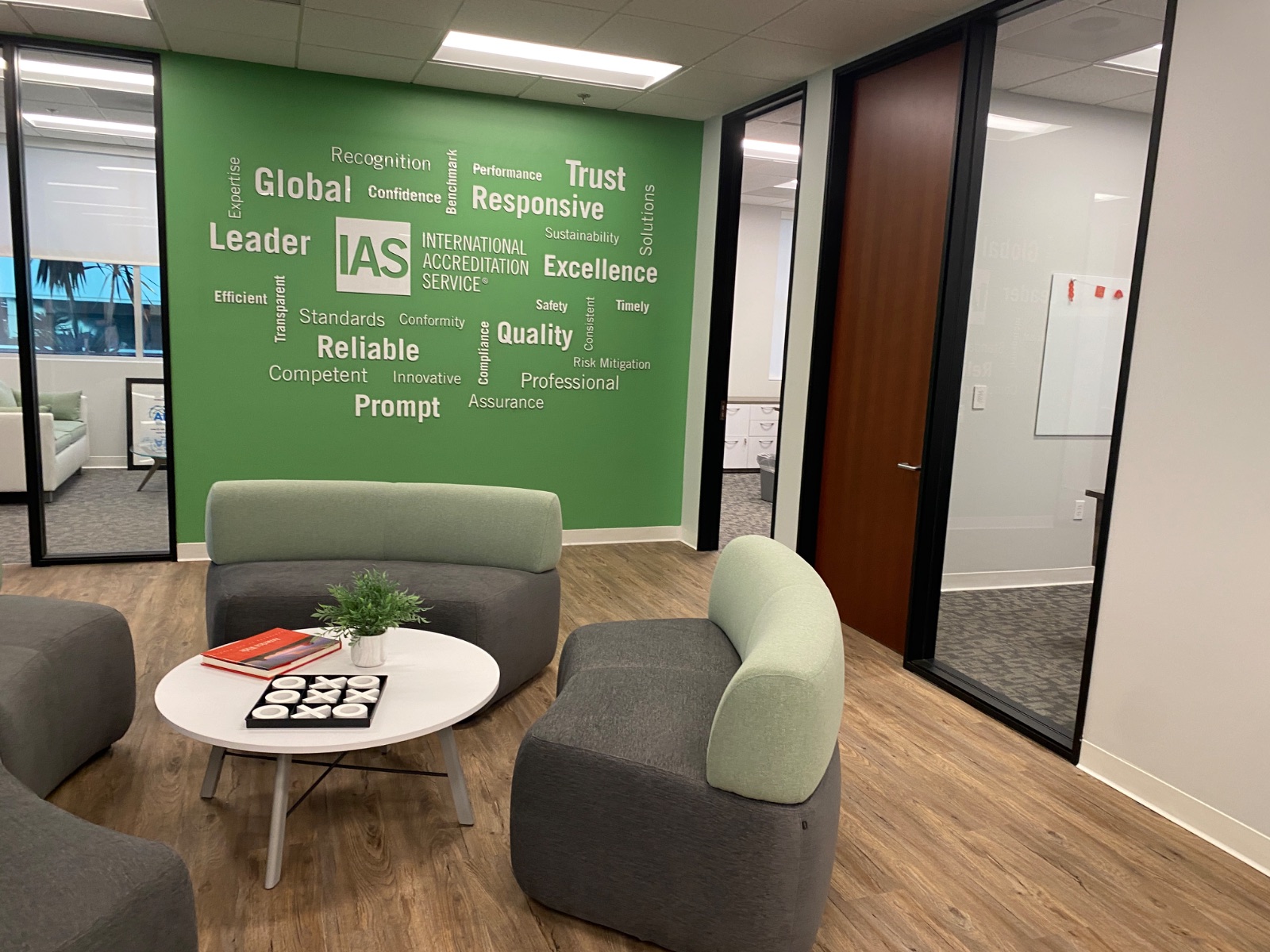 Office lounge with grey and green soft seating in front of the green cut-vinyl word-cloud wall, installed by Hi Sign, Brea, CA