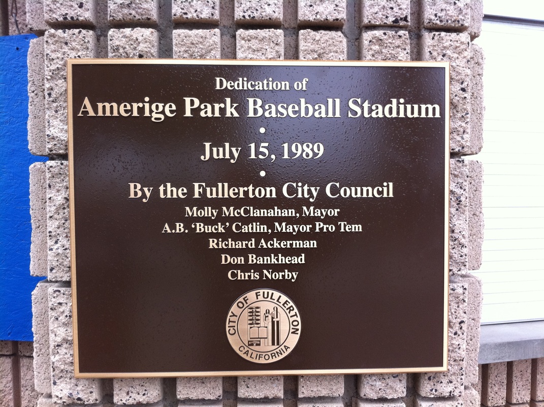 Bronze-tone dedication plaque with raised cream lettering reading 'Dedication of Amerige Park Baseball Stadium, July 15, 1989, By the Fullerton City Council' with council member names and the City of Fullerton seal, mounted on a split-face block wall, installed by Hi Sign, Brea, CA