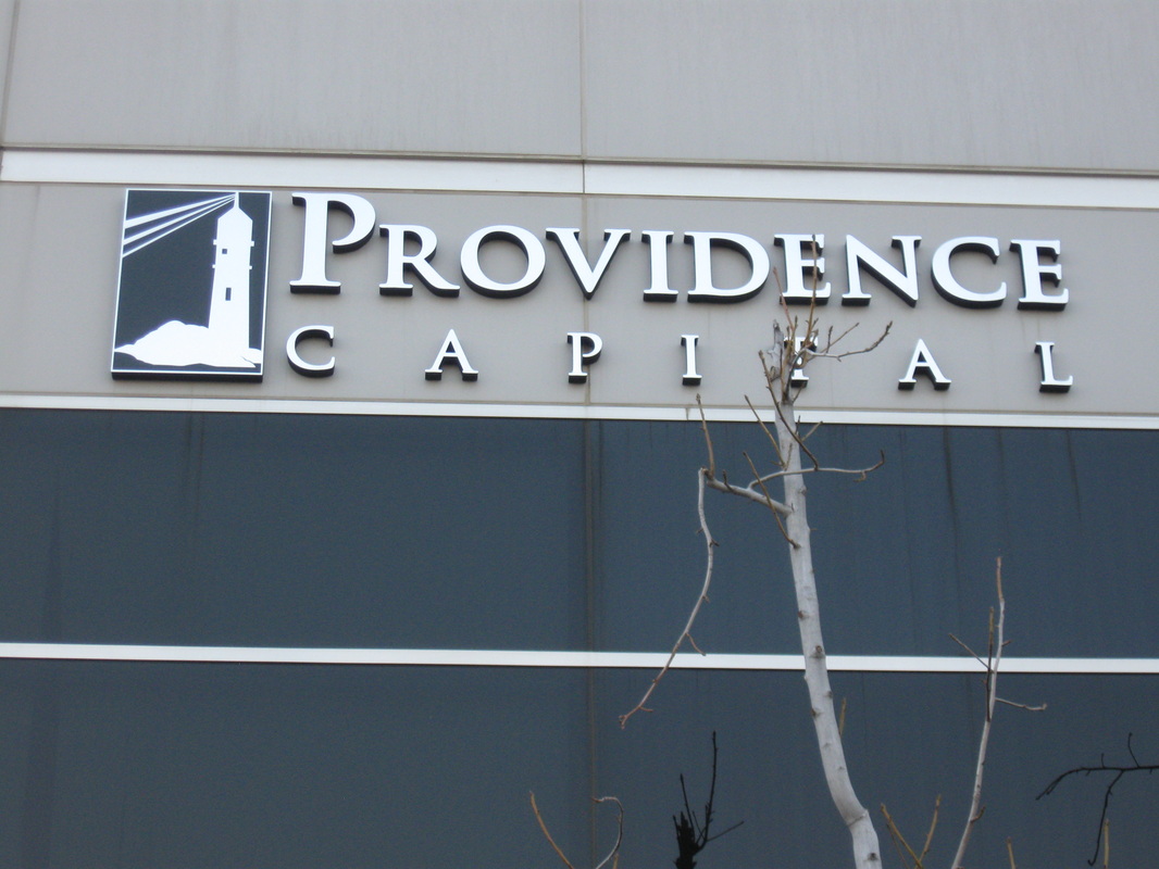 Exterior building fascia for Providence Capital: white dimensional letters spelling PROVIDENCE CAPITAL beside a black-and-white lighthouse logo panel, mounted on a gray precast band above dark glazing, installed by Hi Sign, Brea, CA